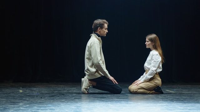 A man and a woman kneeling facing each other on a theatre stage